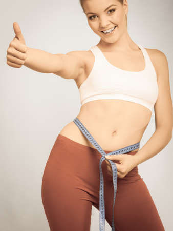 Time for diet slimming weight loss. Fitness woman fit girl with measure tape measuring her waistline showing thumb up success hand gestureの写真素材