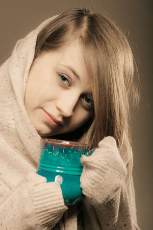 Hot beverage. Sleepy girl holding cup mug of drink tea or coffee. Woman in warm sweater warming herselfの写真素材