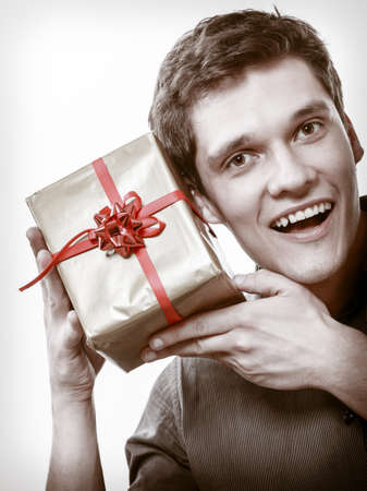 Holiday and special occasion. Young handsome man got golden present gift box with red ribbon isolated on white. Surprise. Studio shot.の写真素材
