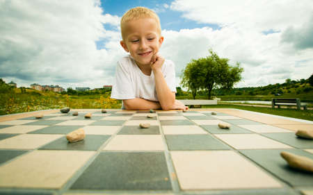 Draughts board game. Little boy clever child kid playing checkers thinking, outdoor in the park. Childhood and developmentの写真素材