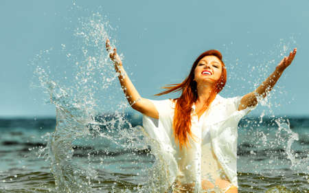 Vacation. Girl splashing water on the coast. Young woman having fun relaxing on the sea. Summertime.