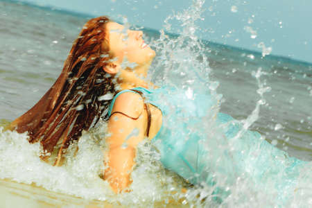 Vacation. Sensual girl wet cloth in water on the coast. Redhair woman having fun relaxing on the sea. Summertime.の写真素材