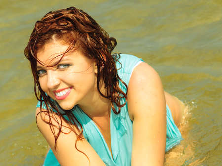 Vacation. Sensual girl wet cloth in water on the coast. Redhair woman having fun relaxing on the...