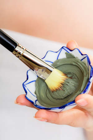 Skin care. Closeup of cosmetic. Woman with brush applying clay mask on face. Girl taking care of dry compexion. Spa.の写真素材