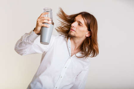 Young stylish man bartender with shaker making alcohol cocktail drink studio shot on gray