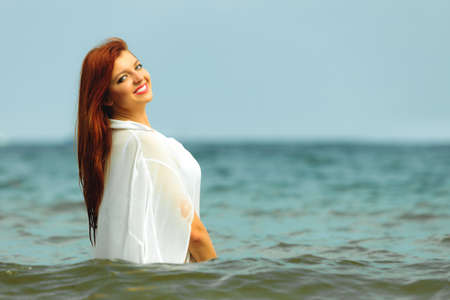 Vacation. Sensual girl wet cloth in water on the coast. Redhair woman having fun relaxing on the sea. Summertime.の写真素材