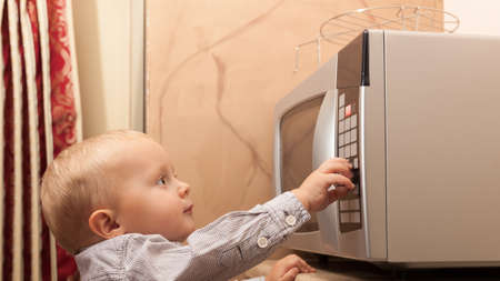Little boy child kid playing with timer of microwave oven kitchenware in the domestic kitchen at home.の写真素材