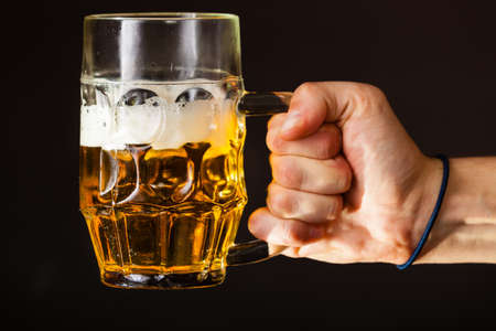 Male hand holding mug of beer dark backgroundの写真素材