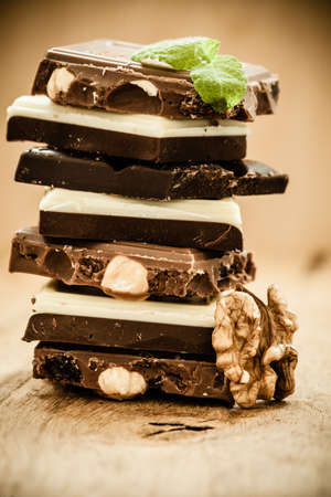 Closeup stack of different sorts chocolate pieces and walnut. Variety of chocolates on wooden table.
