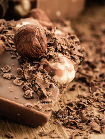 Closeup milk chocolate pieces hazelnuts and shavings curls on wooden table.の写真素材