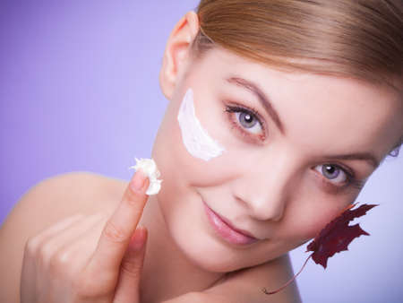 Skincare habits. Face of young woman with leaf as symbol of red capillary skin on gray. Girl taking care of her dry complexion applying moisturizing cream. Beauty treatment.の写真素材