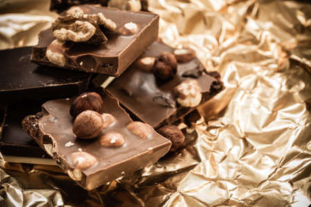 Closeup different sorts chocolate pieces and hazelnuts. Variety of chocolates on golden foil wrapping.の写真素材