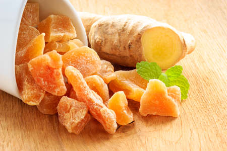 Closeup dried candied crystallized ginger pieces and raw root on wooden table. Healthy food, home remedy for nausea, colds.の写真素材