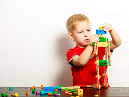 Little blond boy child kid preschooler playing with colorful building blocks toys interior. At home....