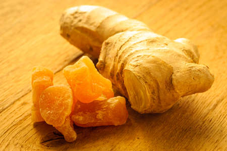 Closeup dried candied crystallized ginger pieces and fresh root on wooden table. Healthy food, home...