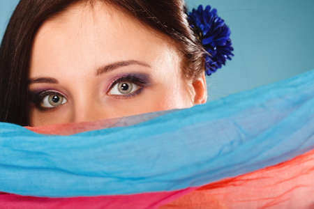 Young woman makeup on eyes hiden her face with multicolored shawl blue backgroundの写真素材