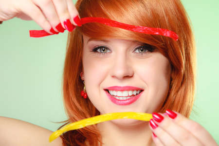 Sexy young woman holding candy. Redhair cute funny girl framing her face with sweet jelly on greenの写真素材
