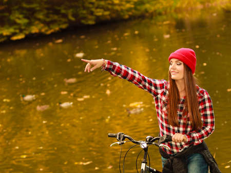 Fall active lifestyle concept,. young woman sporty casual girl relaxing in autumnal park with bicycle pointing with hand, outdoorの写真素材