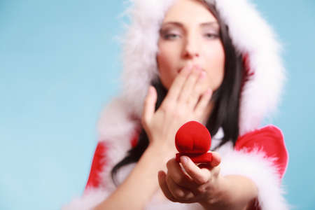 Surprised happy girl young woman wearing santa claus costume opening present red heart shaped gift box with engagement ring on blue background. Christmas time gifts.の写真素材