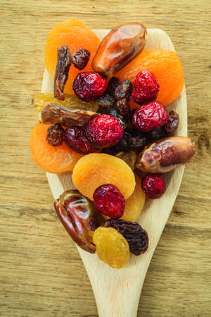 Healthy high fiber food, organic nutrition. Closeup different varieties mix of dried fruits on wooden spoon.の写真素材