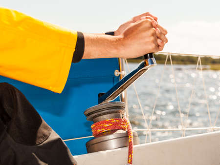 Male hand on winch capstan with rope on sailing boat. Yachting yacht in blue baltic sea sunny day...