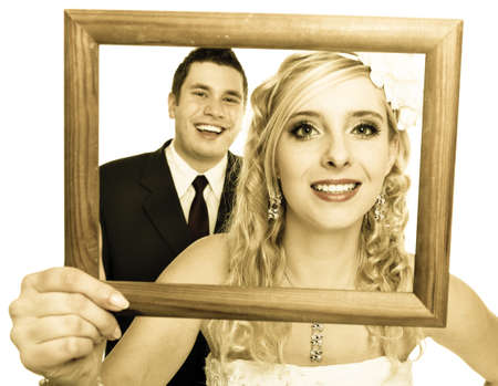 Wedding day. Portrait of happy bride woman girl and groom man couple in wooden frame isolated on white. Studio shot.の写真素材