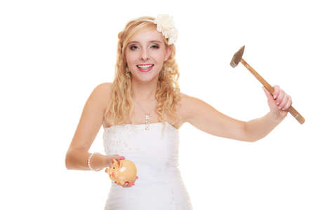 Money saving, marriage and high wedding cost concept. Funny woman bride with hammer about to smash piggy bank isolated on whiteの写真素材