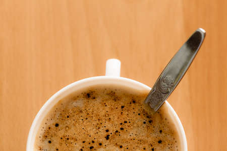 Beverage. Closeup of cup of hot drink coffee cappuccino with froth and teaspoon on wooden table...