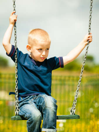 Little blonde boy having fun at the playground. Child kid playing on a swing outdoor. Happy active childhood.の写真素材