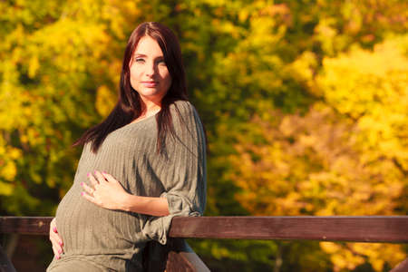 Pregnancy, motherhood and happiness concept. Relaxed calm pregnant woman walking outside in autumn parkの写真素材