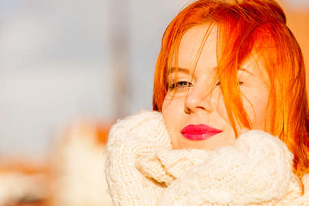 Winter fashion. Beauty face portrait redhaired young woman in warm clothing outdoor enjoying sunlight on sunny day.の写真素材