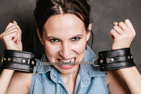 Arrest and jail. Criminal angry woman prisoner girl showing leather handcuffs on gray. Punishment.の写真素材