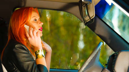 Concept of danger driving. Young woman driver redhaired girl talking on mobile phone smartphone...
