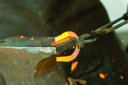 Making decorative element in the smithy on the anvil. Hammering glowing steel. Blacksmith forges a...