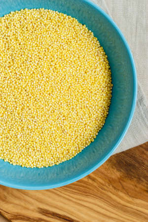 Dieting healthcare concept. Millet groats in blue bowl on wooden table. Healthy food high protein content.の写真素材