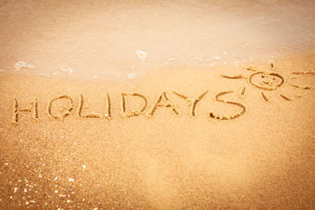 Summer vacation concept. The word holidays written in the sand on beach.の写真素材