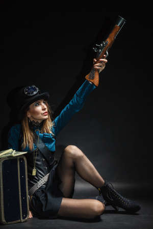 Criminal story bad girl steampunk retro woman with bag suitcase and gun studio shot grunge dark...