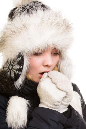 Winter vacation. Freezing girl in warm clothes. Young woman in fur hat warming her cold hands by breath isolated on white.の写真素材