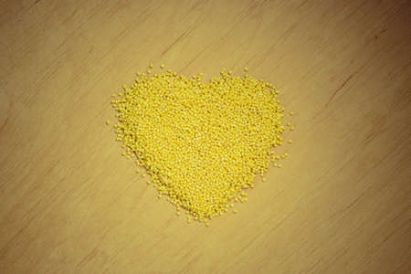Dieting healthcare concept. Millet groats heart shaped on wooden surface. Healthy food gluten-free and highly alkaline.の写真素材