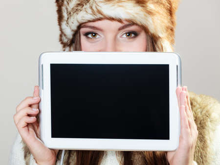 Technology internet concept. fashion woman in winter clothes covering her face with computer, showing blank copy space on screen tablet touchpad studio shot on grayの写真素材