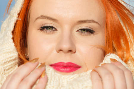 Winter fashion. Close up beauty face portrait red hair young woman in warm clothing white hood on head outdoor enjoying sunlight on sunny day.の写真素材