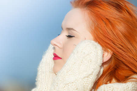 Winter fashion. Beauty face portrait red hair young woman in warm clothing outdoor enjoying sunlight on sunny day.の写真素材