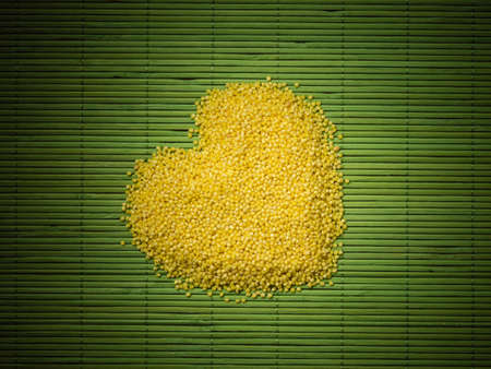 Dieting healthcare concept. Millet groats heart shaped on green straw mat surface. Healthy food non gluten grain.の写真素材