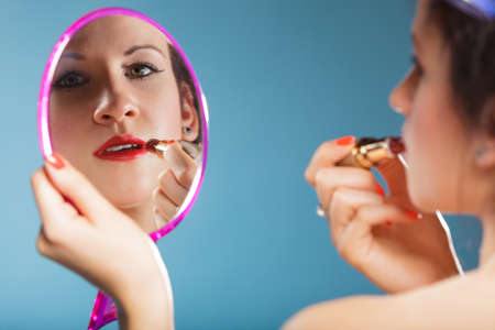 Cosmetic beauty procedures and makeover concept. Closeup part of woman face. Girllooking at mirror applying red lipstick lips makeupの写真素材