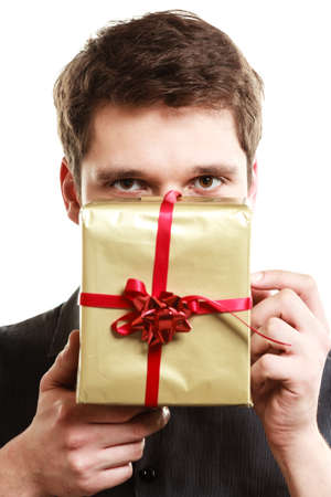 Holiday and special occasion. Young handsome man giving golden gift box with red ribbon isolated on white. Guy covering his face with present. Surprise. Studio shot.の写真素材
