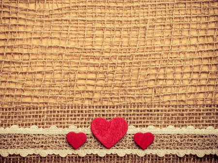 Valentines day or wedding concept. Red wooden decorative hearts lace ribbon on abstract cloth burlap...