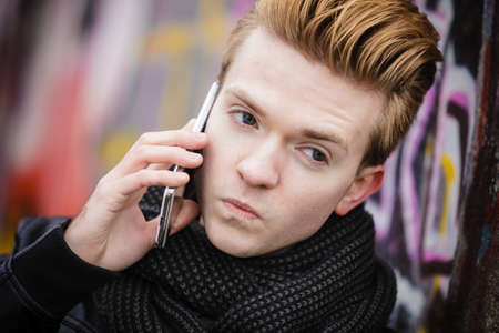 Technology and communication. Closeup young fashion man talking on mobile cell phone using smartphone outdoor graffiti wall backgroundの写真素材