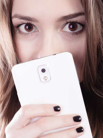 Technology and communication. Closeup young woman teenage girl covering her face with mobile phone, using smartphone.の写真素材