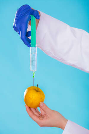 Genetic modification concept. Human hand holding fruit and syginge. Apple receiving an injection of some substance for rapid ripening.の写真素材