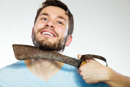 Handsome man bearded guy shaving with very large knife on gray background. Humour